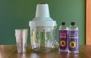 Reviewing the Resiners Airless Bubble Removal Machine - showing the machine next to some resin mixture and the hardener, as well as the cups included with the product.