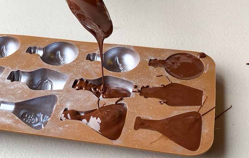 Pouring chocolate into a silicone mould with bottle shapes. Making halloween chocolate candy