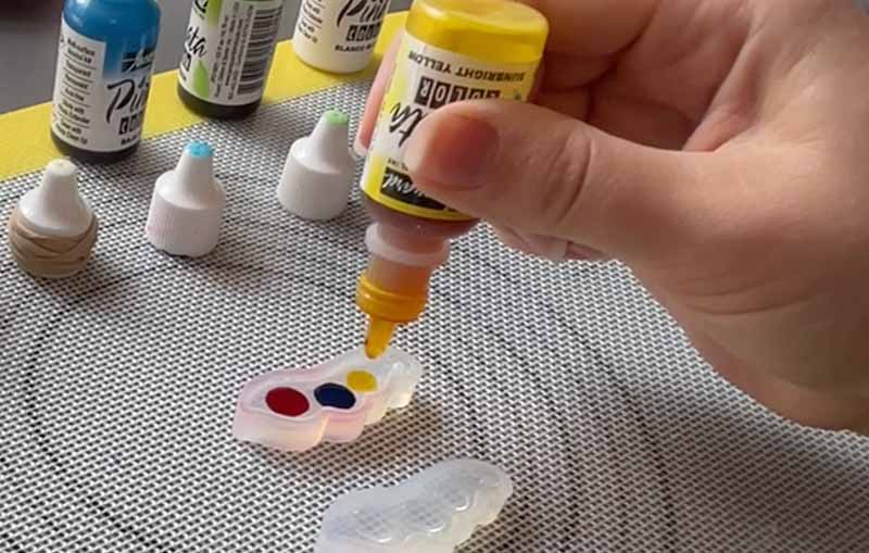 Resin artist using yellow alcohol ink to fill a silicone mould