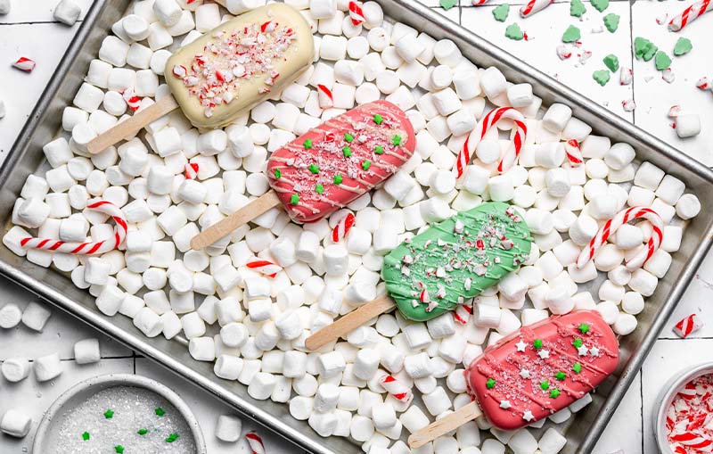 Christmas themed cakesicles on a bed of small marshmallows