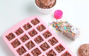 Large Pink silicone mold filled with chocolate brownie mix next to a jar of coloured sprinkles