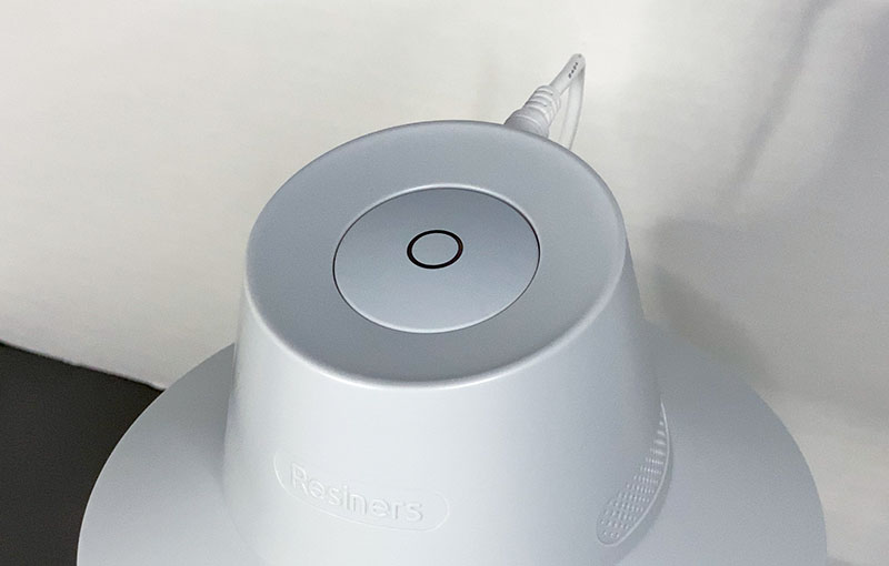 Close-up of the Resiners Airless Lite's single control button on the grey surface with the brand name visible, indicating a sleek and user-friendly design.