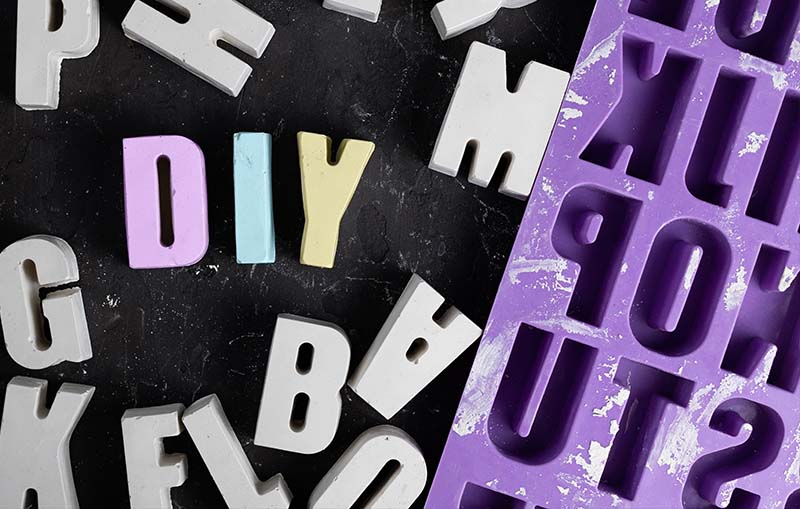 Assorted concrete letters spread out next to a purple silicone alphabet mold used for creating them, showcasing the concept of 'Silicone Molds with Concrete