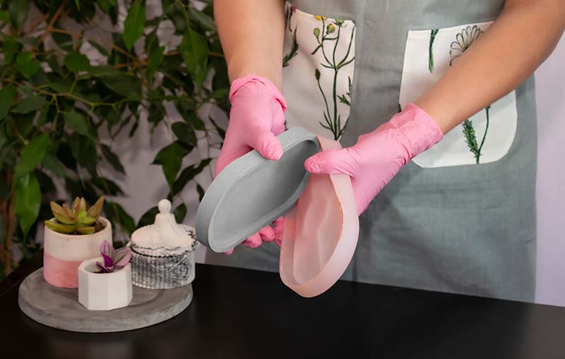 Person wearing pink gloves removing a newly cast concrete piece from a flexible silicone mold, highlighting 'Silicone Molds with Concrete