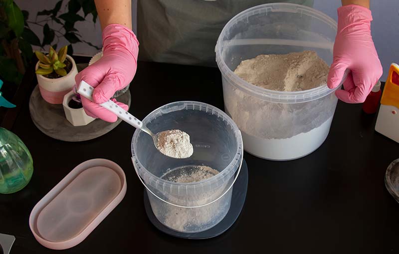 Measuring and preparing concrete mix ingredients next to pink silicone molds, part of the 'Silicone Molds with Concrete' process.
