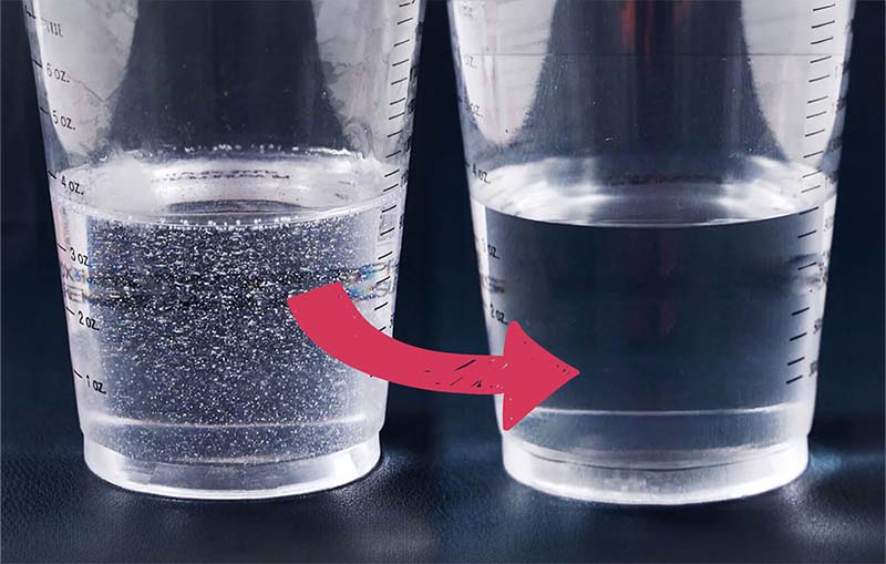 Two measuring cups with clear resin; the left cup has bubbles throughout, indicated by an arrow pointing to the right cup, which has no bubbles, demonstrating a step in preparing silicone molds for resin.