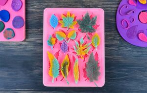 Clay for silicone molds - Pink silicone mold with assorted leaf shapes filled with colorful clay leaves on a dark wooden background.