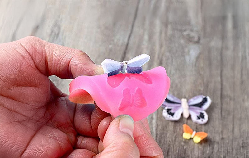 Clay for silicone molds - Demolding a butterfly-shaped clay piece from a pink silicone mold.